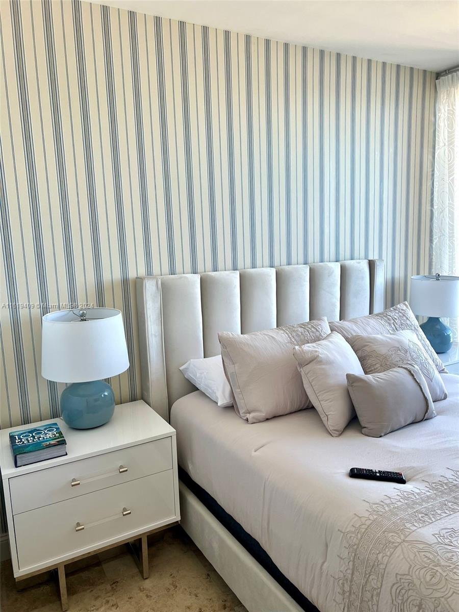 A bedroom features a tufted headboard, striped wallpaper, and a white nightstand with a lamp — 6365 Collins Ave # 2610, Miami Beach FL 33141, MIAMI BEACH, FL