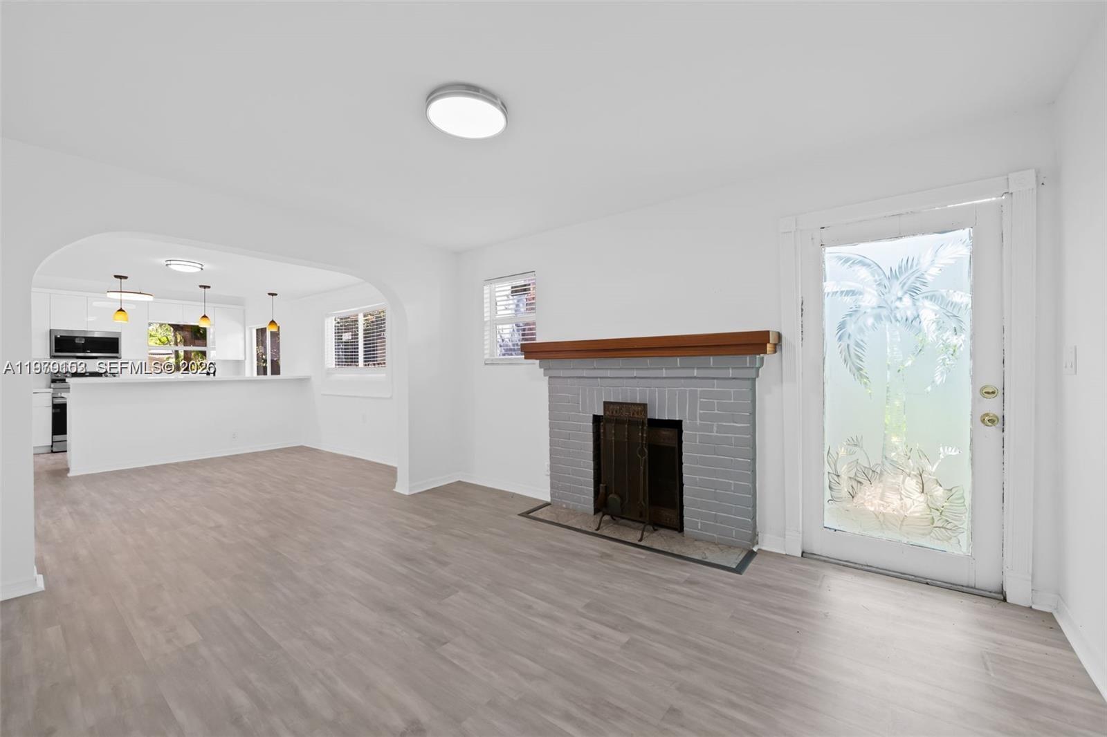 A living room features a gray brick fireplace, light wood-look flooring, and an arched entryway — 1640 Funston St, Hollywood FL 33020, HOLLYWOOD, FL