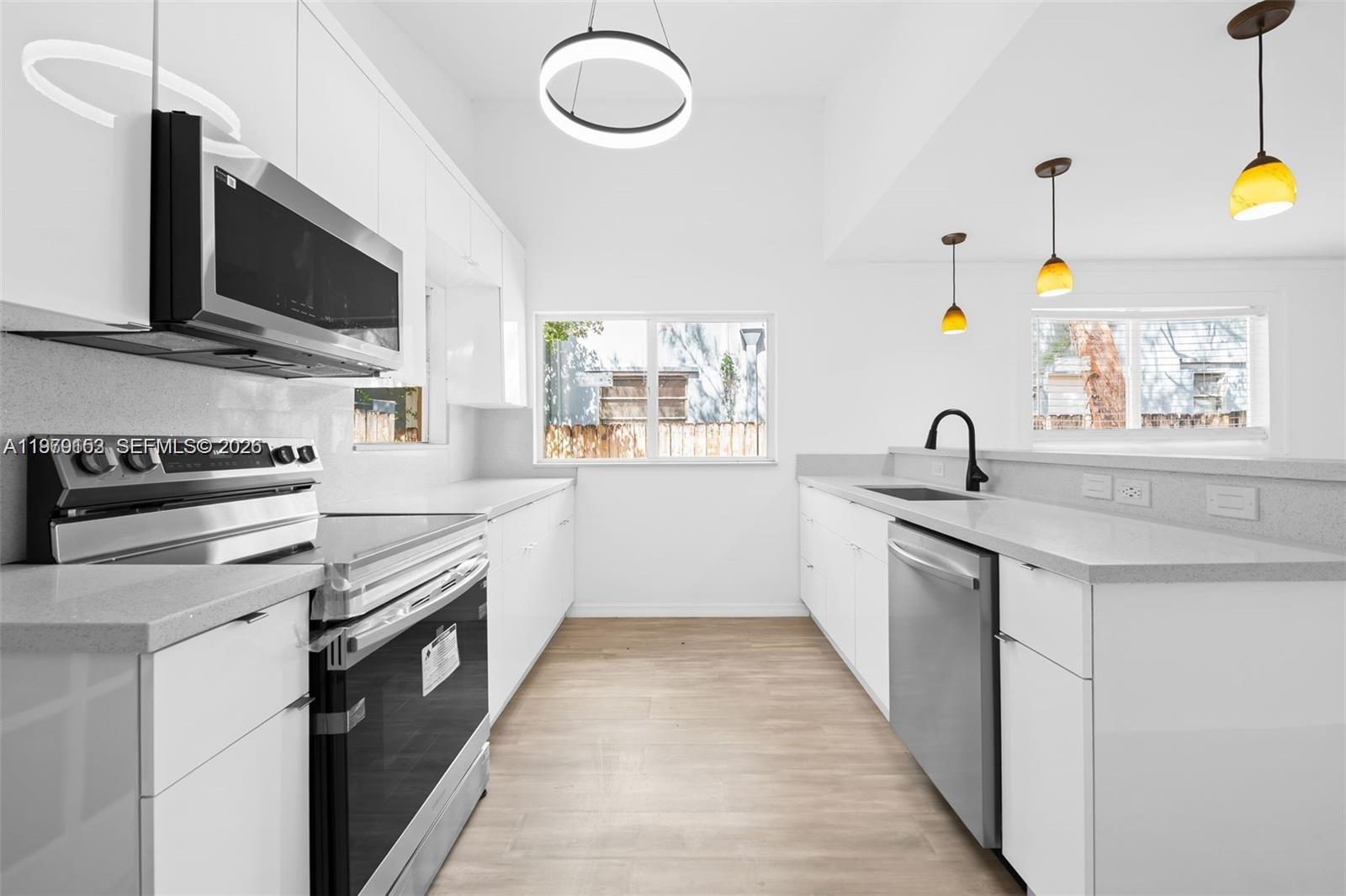 A modern kitchen features white cabinetry, stainless steel appliances, and light wood-look flooring — 1640 Funston St, Hollywood FL 33020, HOLLYWOOD, FL