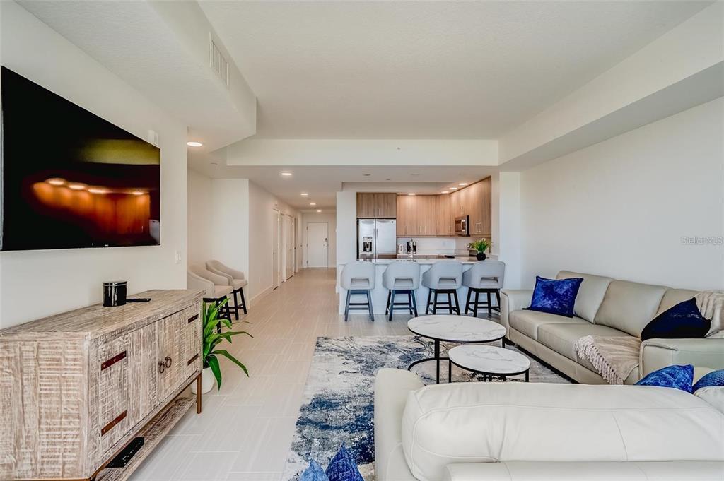 An open-concept living room and kitchen featuring light tile floors and modern neutral furnishings — 415 ISLAND WAY UNIT 311, CLEARWATER, FL