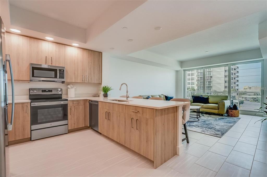 A modern kitchen with light wood cabinets and a central island overlooks a living area — 415 ISLAND WAY UNIT 311, CLEARWATER, FL