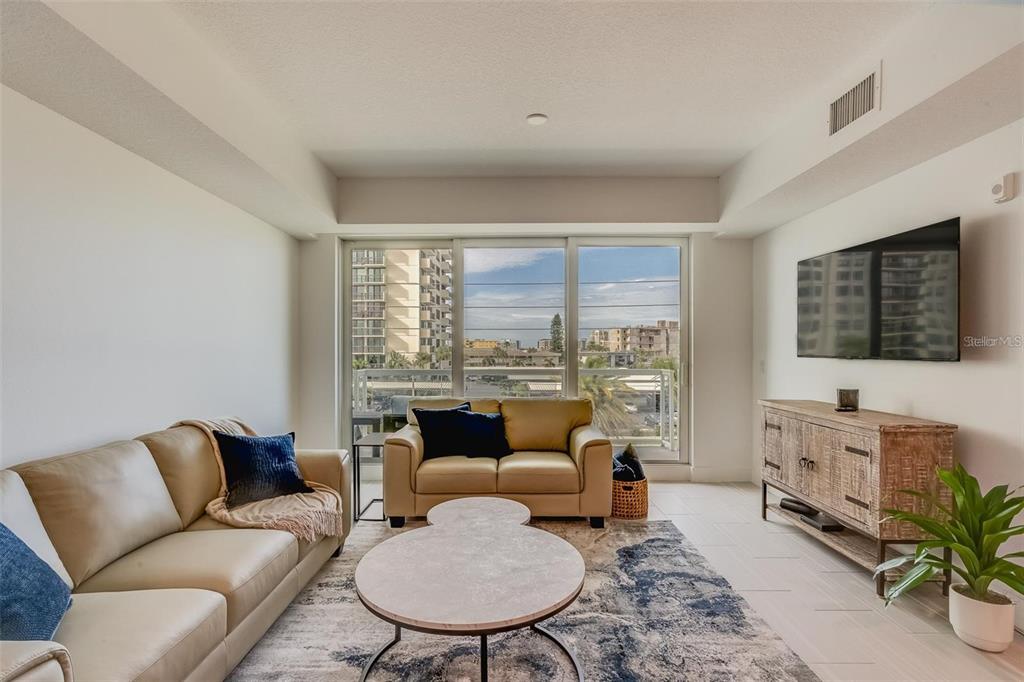 A living room features tan leather sofas, a patterned area rug, and a large window — 415 ISLAND WAY UNIT 311, CLEARWATER, FL