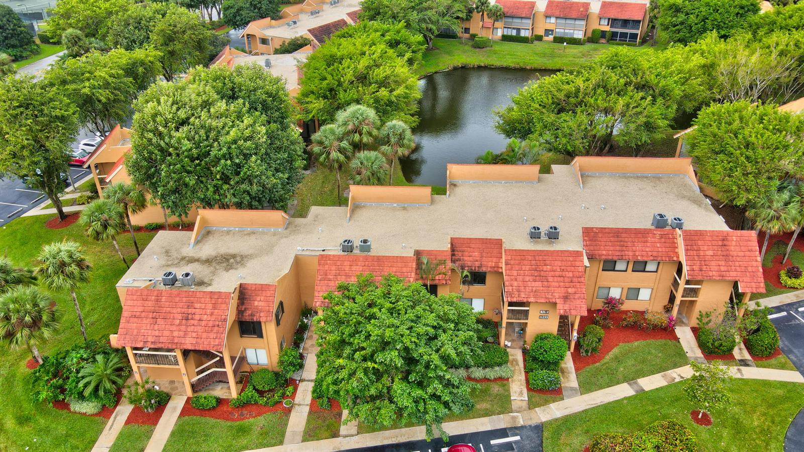 An aerial view of a multi-unit residential building with a pond and surrounding trees — 11255 Green Lake Drive # 202, Boynton Beach FL 33437, BOYNTON BEACH, FL