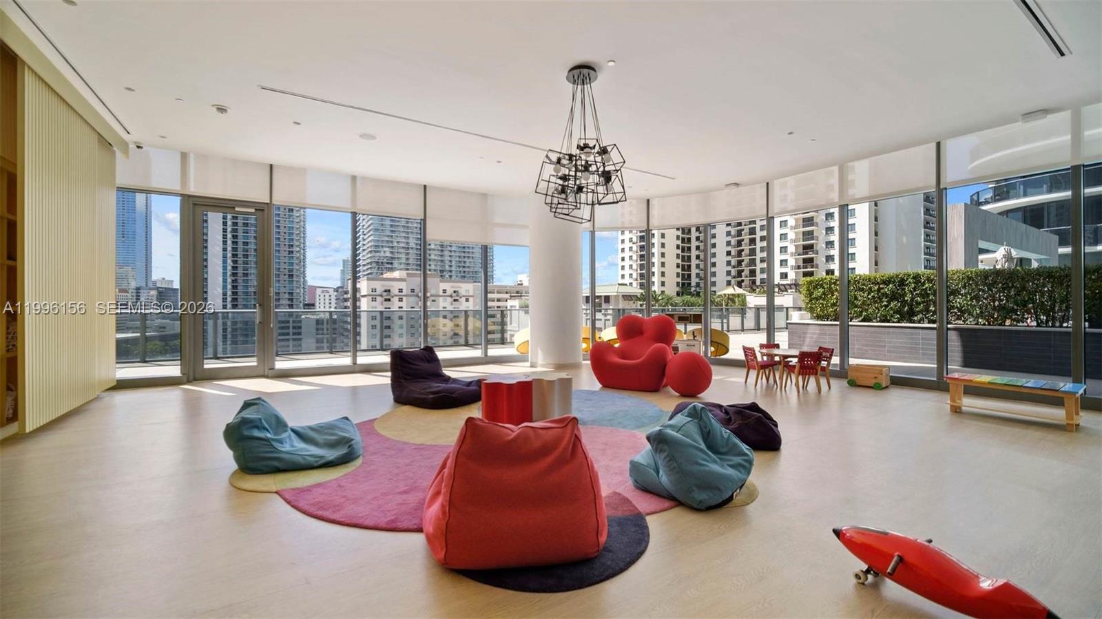 A brightly lit playroom features beanbag chairs, a red lounge chair, and floor-to-ceiling windows — 55 SW 9th # 2804, Miami FL 33130, MIAMI, FL
