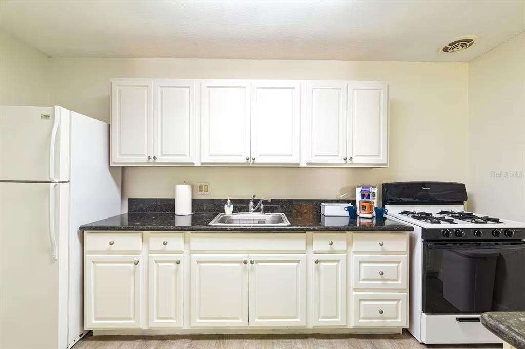 A kitchen features white cabinets, dark countertops, a stainless steel sink, and white appliances — 1700 SW 16TH COURT UNIT K24, GAINESVILLE, FL