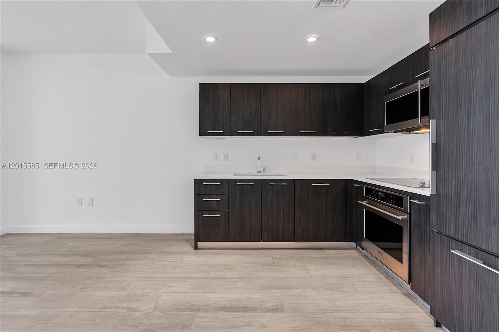 A modern kitchen features dark wood cabinetry, stainless steel appliances, and light-colored tile flooring — 45 SW 9th St # 3502, Miami FL 33130, MIAMI, FL