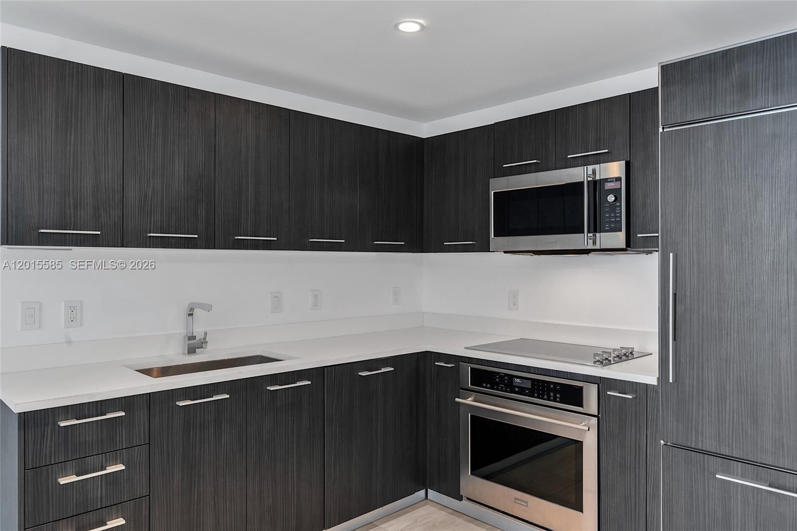 A modern kitchen features dark wood-grain cabinets, stainless steel appliances, and white countertops — 45 SW 9th St # 3502, Miami FL 33130, MIAMI, FL