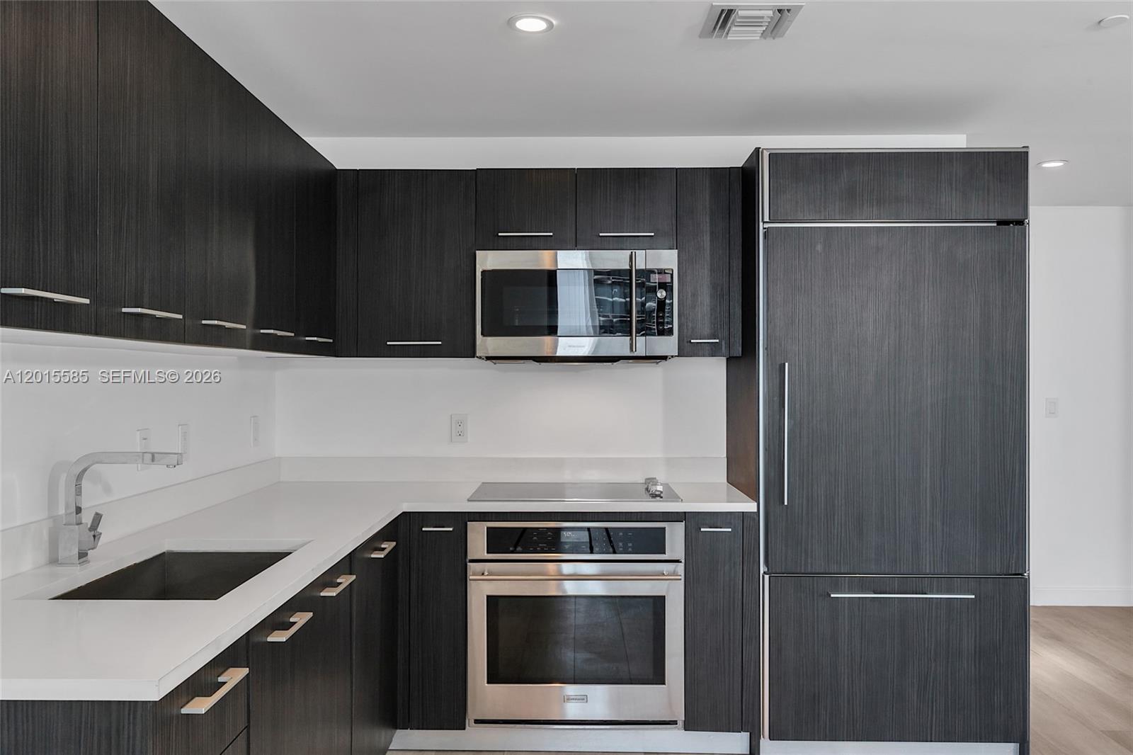 A modern kitchen features dark wood cabinetry, stainless steel appliances, and white countertops — 45 SW 9th St # 3502, Miami FL 33130, MIAMI, FL