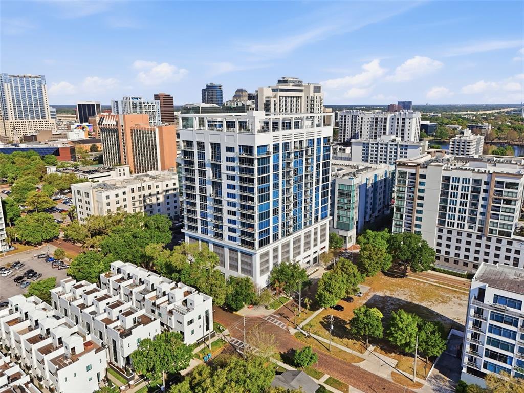 An aerial view of a tall, modern white apartment building surrounded by urban city buildings — 260 S OSCEOLA AVENUE UNIT 902, ORLANDO, FL
