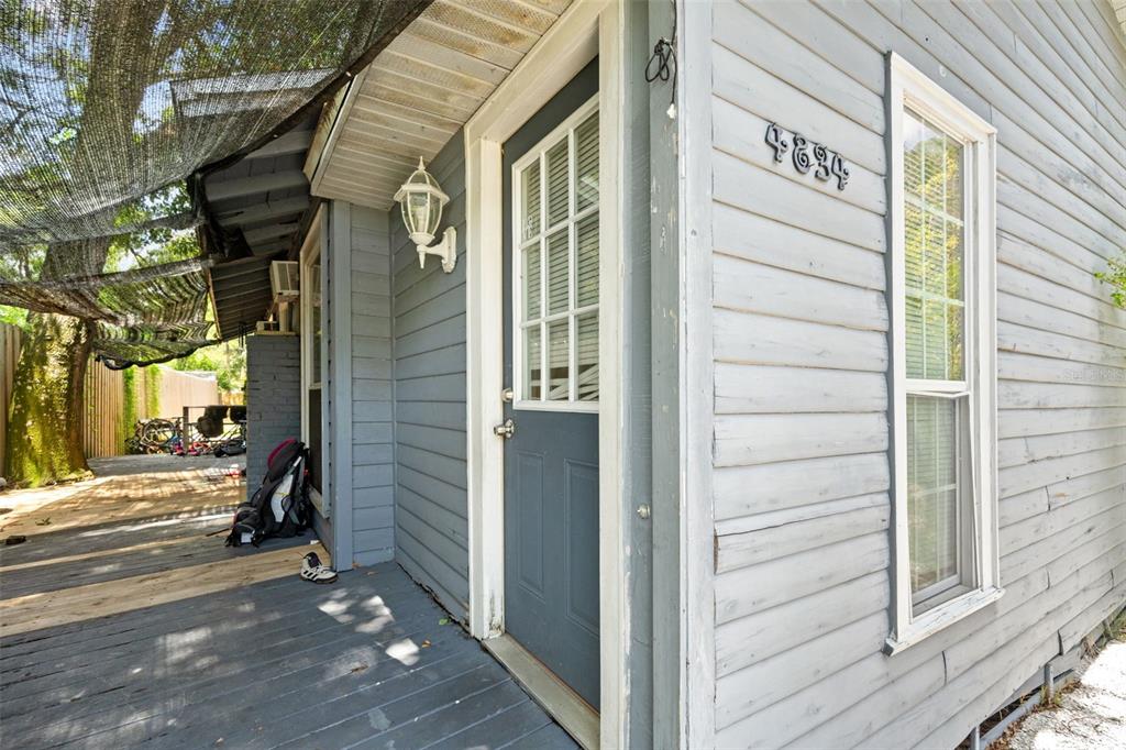 A gray house exterior features a wooden porch, a dark door, and a white-framed window — 4834 TAYLOR STREET N, ST PETERSBURG, FL