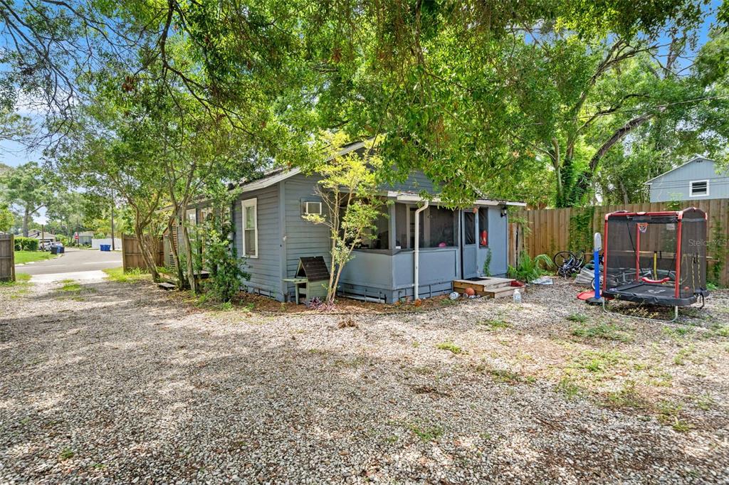 A gray, single-story house with a screened-in porch sits on a gravel lot with trees — 4834 TAYLOR STREET N, ST PETERSBURG, FL