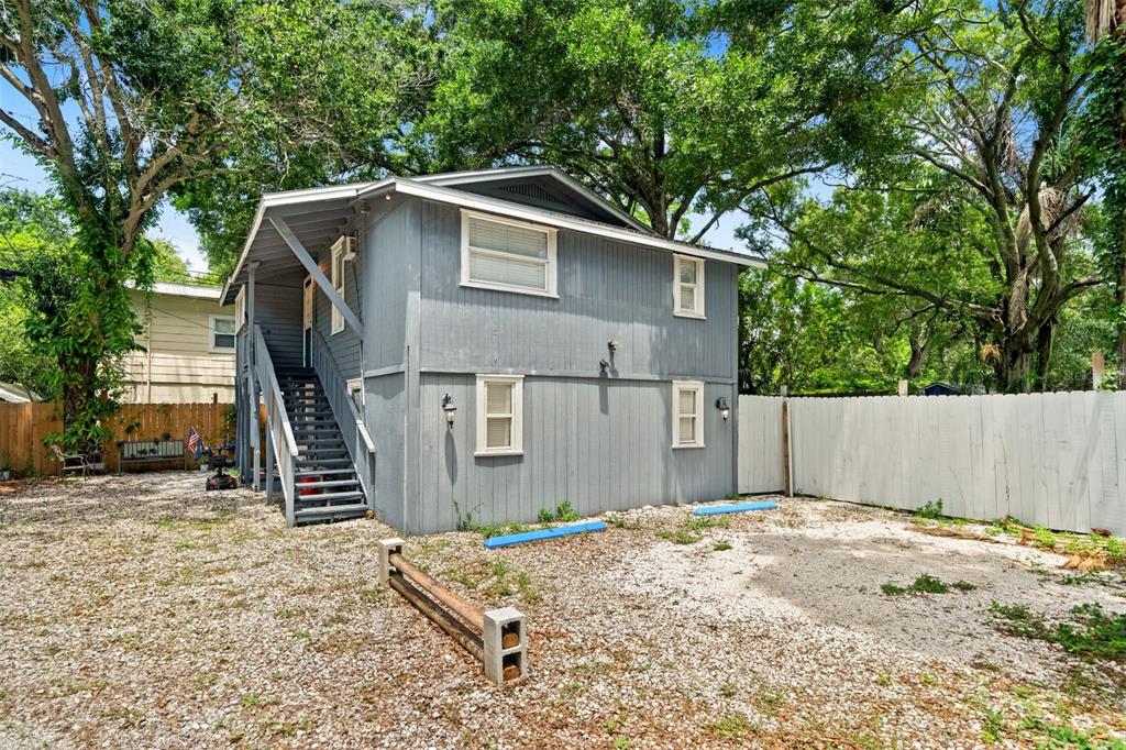 A two-story grey house with an exterior staircase stands on a gravel lot — 4834 TAYLOR STREET N, ST PETERSBURG, FL