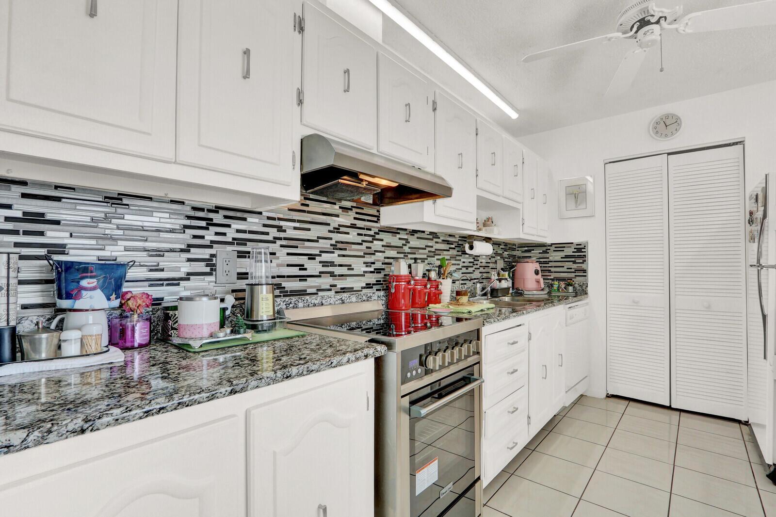 A kitchen with white cabinets, granite countertops, a stainless steel stove, and a tiled backsplash — 615 Laconia Circle # A, Lake Worth FL 33467, LAKE WORTH, FL