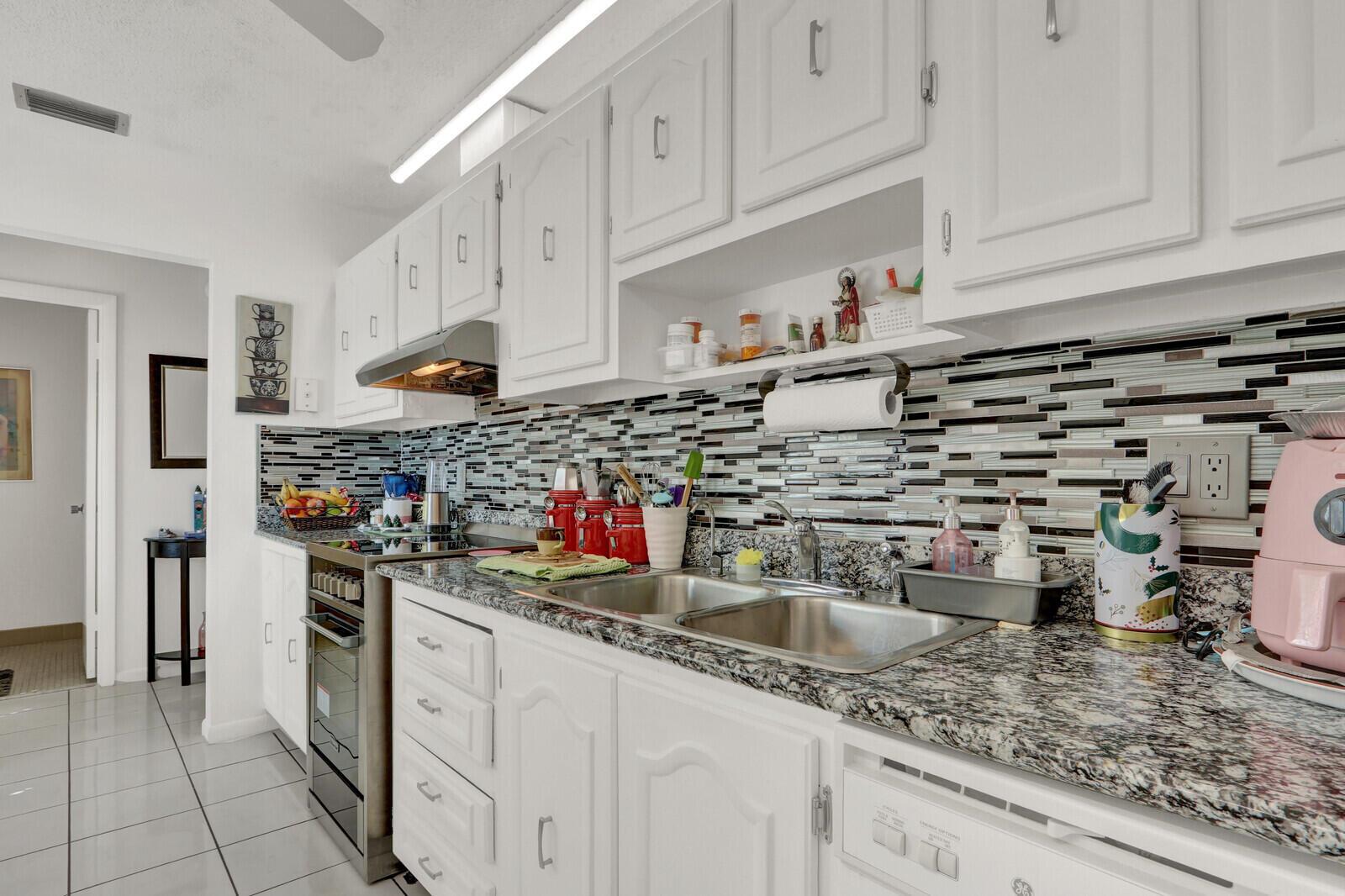 A kitchen with white cabinets, granite countertops, a stainless steel sink, and a tiled backsplash — 615 Laconia Circle # A, Lake Worth FL 33467, LAKE WORTH, FL
