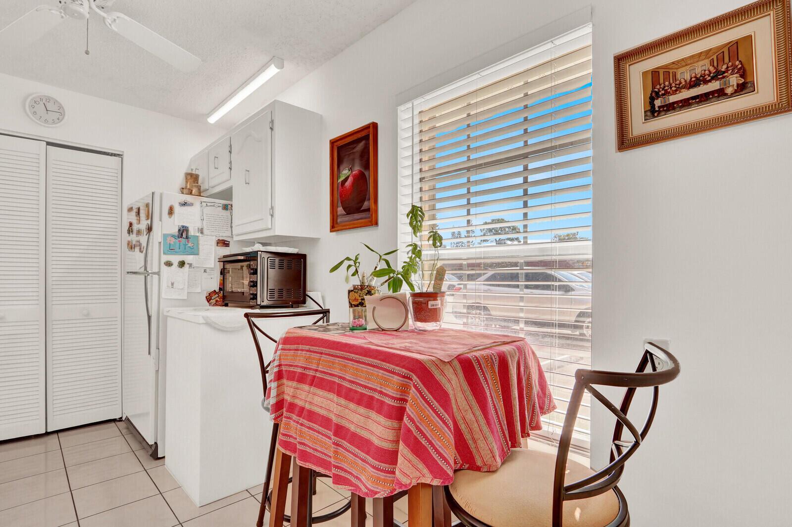 A small kitchen features a dining table by a window, white cabinets, and tiled floors — 615 Laconia Circle # A, Lake Worth FL 33467, LAKE WORTH, FL