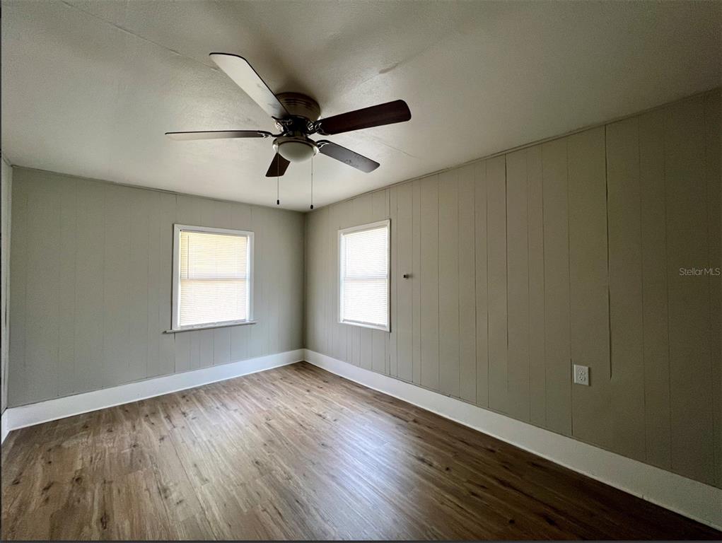 An empty bedroom features wood-look flooring, light-colored paneled walls, two windows, and a ceiling fan — 2003 10TH STREET S, ST PETERSBURG, FL