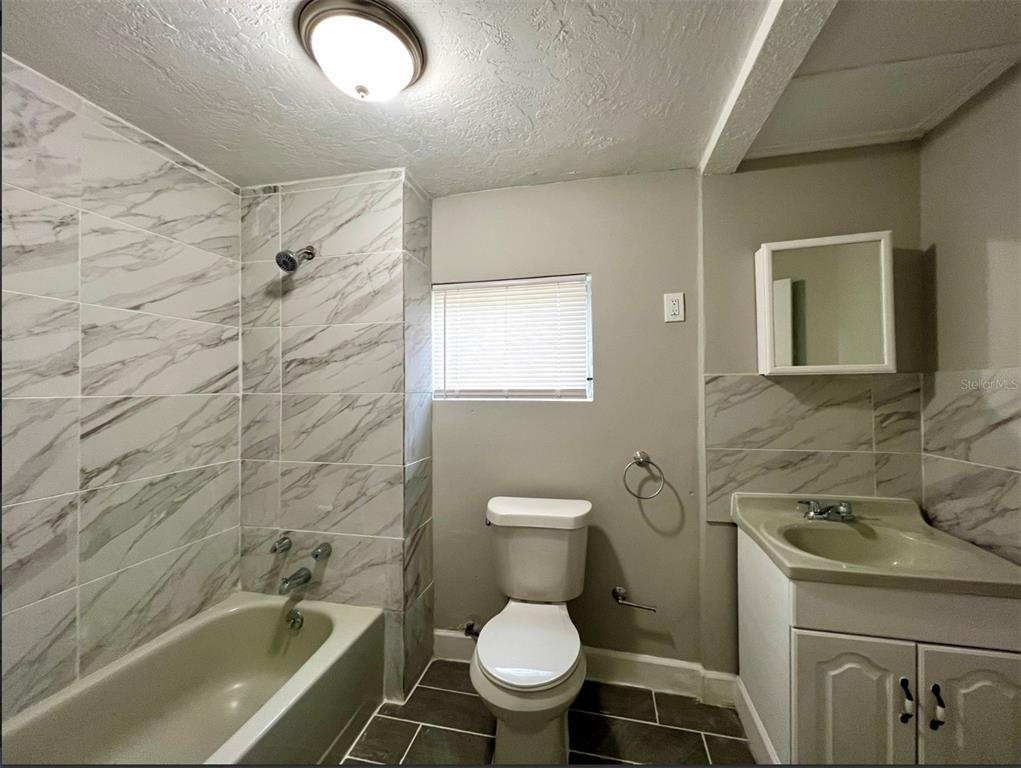 A bathroom featuring a marble-tiled shower surround, a white vanity, and a toilet — 2003 10TH STREET S, ST PETERSBURG, FL