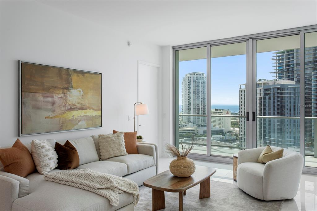 A modern living room with a sectional sofa, coffee table, and floor-to-ceiling windows overlooking cityscapes — 400 CENTRAL AVENUE UNIT 1704, ST PETERSBURG, FL