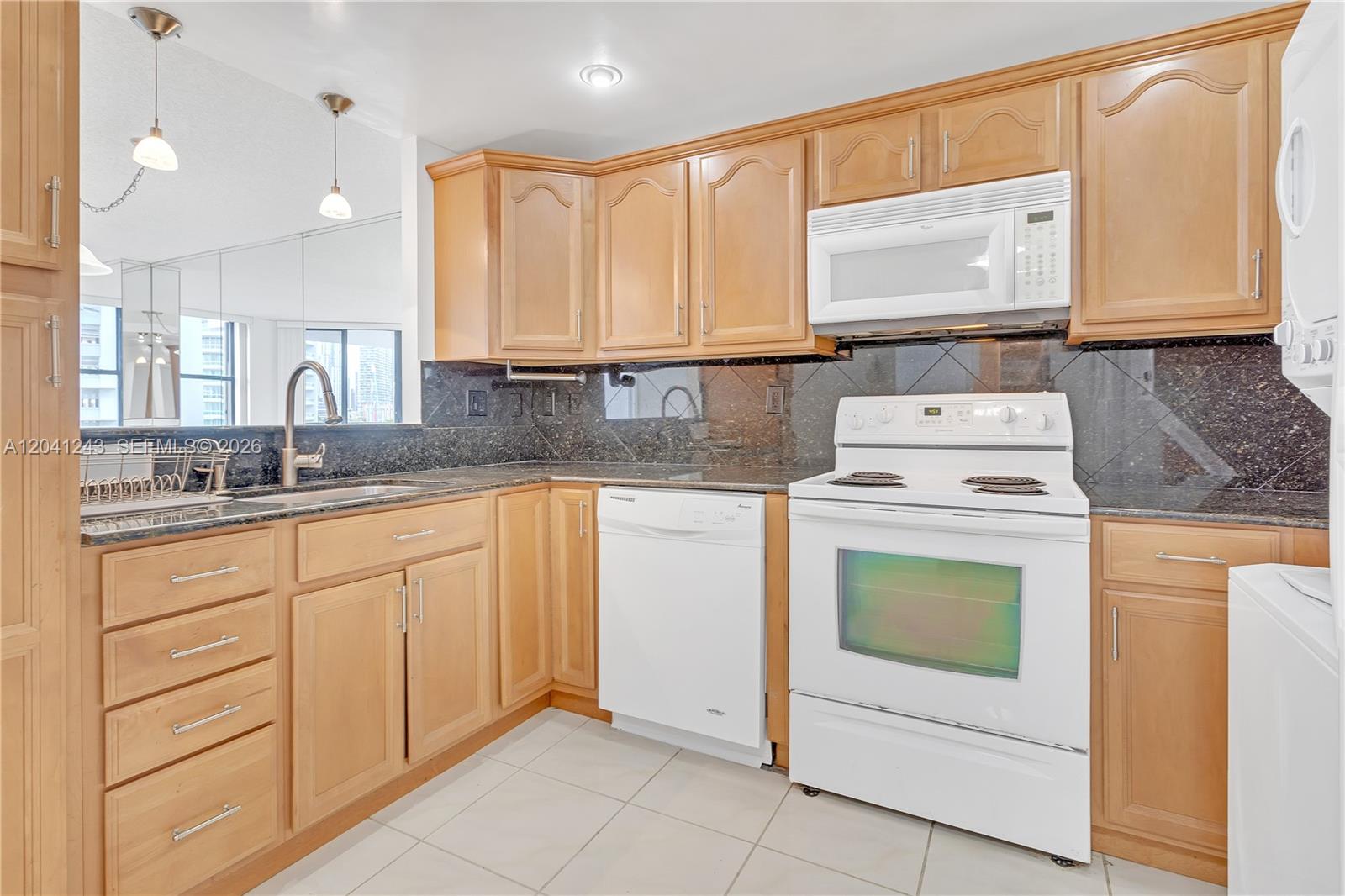 A kitchen features light wood cabinets, dark granite countertops, white appliances, and tiled flooring — 1865 Brickell Ave # A805, Miami FL 33129, MIAMI, FL
