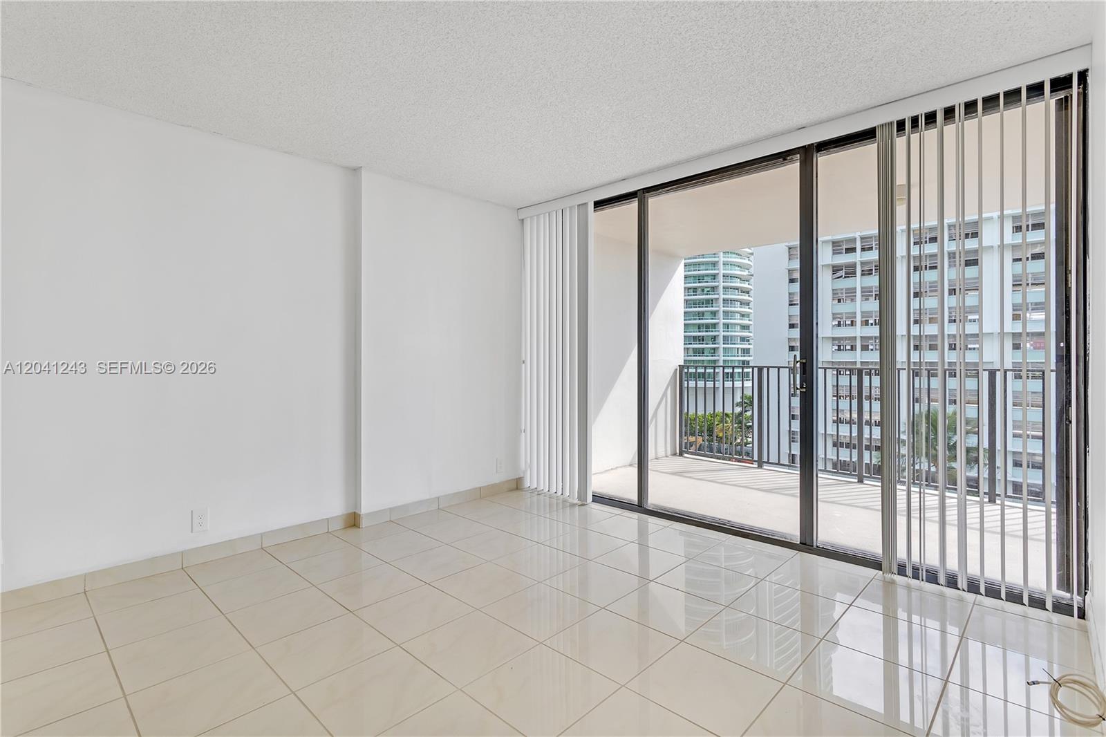 An empty room with beige tile flooring, white walls, and a sliding glass door to a balcony — 1865 Brickell Ave # A805, Miami FL 33129, MIAMI, FL