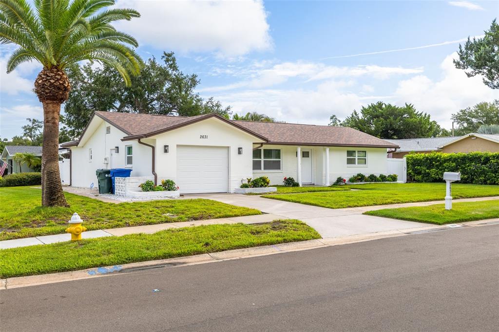 A single-story white house with a garage, palm tree, and lawn under a blue sky — 2631 OAKBROOK DRIVE, LARGO, FL