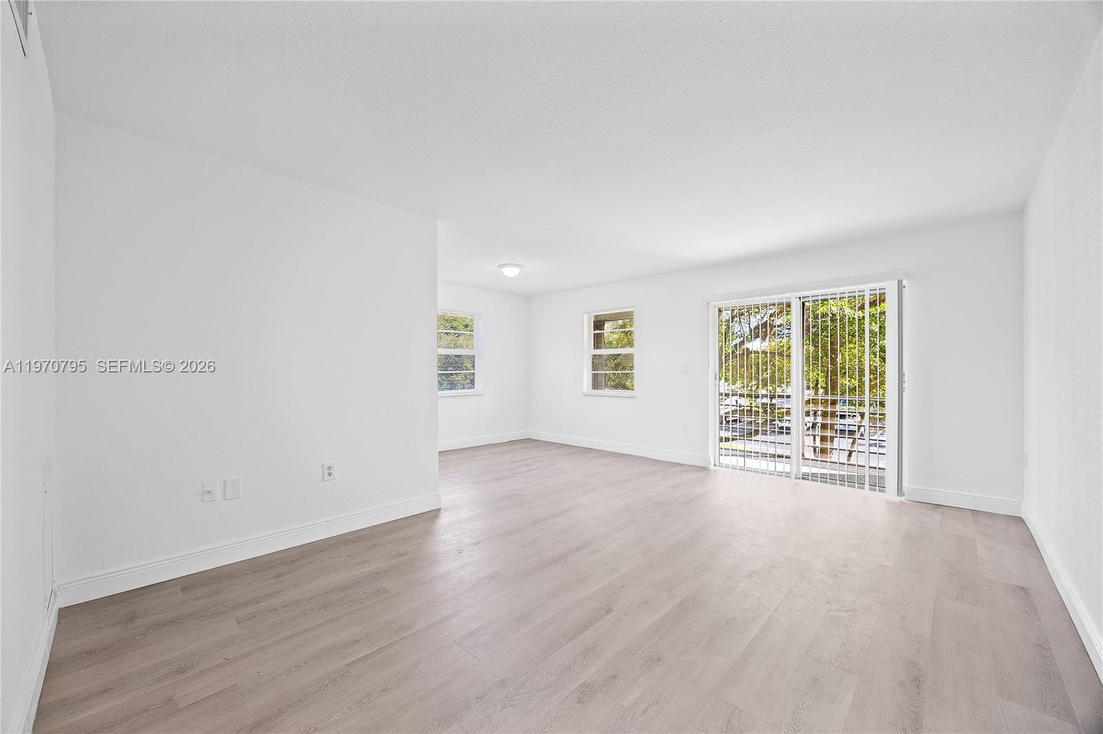 An empty room features white walls, light wood-look flooring, and a sliding glass door — 4990 E Sabal Palm Blvd # 202, Tamarac FL 33319, TAMARAC, FL