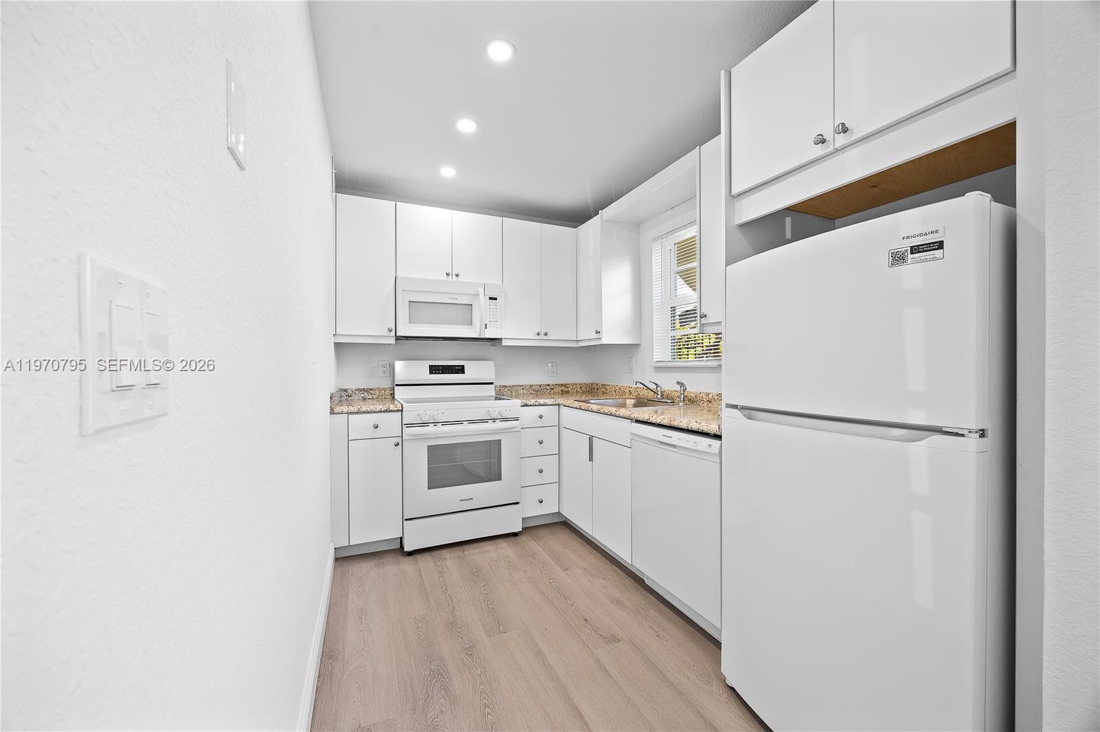 A white kitchen features light wood-look flooring, granite countertops, and white cabinetry — 4990 E Sabal Palm Blvd # 202, Tamarac FL 33319, TAMARAC, FL