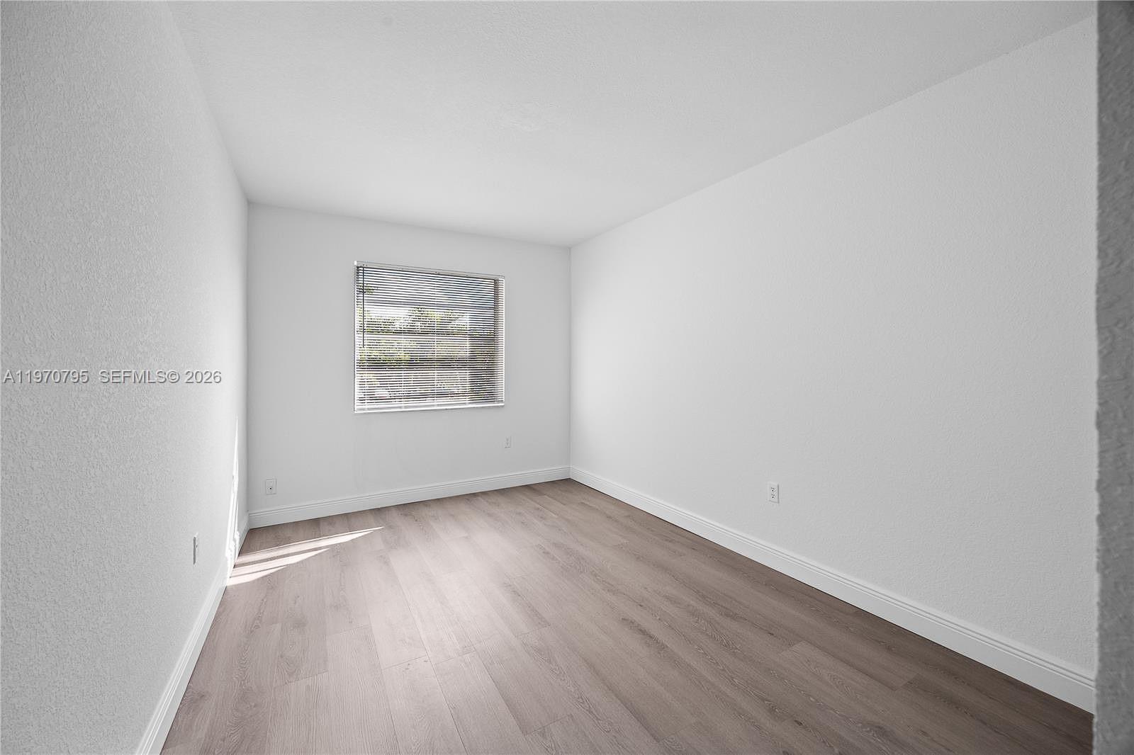 An empty bedroom features white walls, light wood-look flooring, and a single window with blinds — 4990 E Sabal Palm Blvd # 202, Tamarac FL 33319, TAMARAC, FL