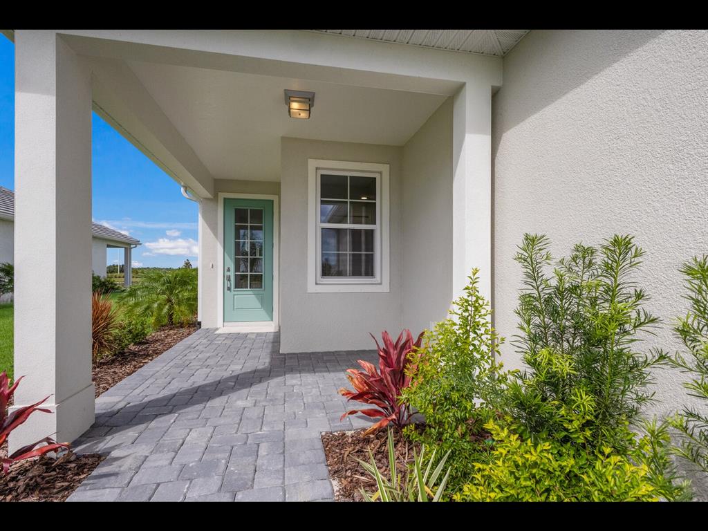A covered front porch with gray pavers, a light green door, and surrounding landscaping — 1099 WATERLINE COURT, SARASOTA, FL
