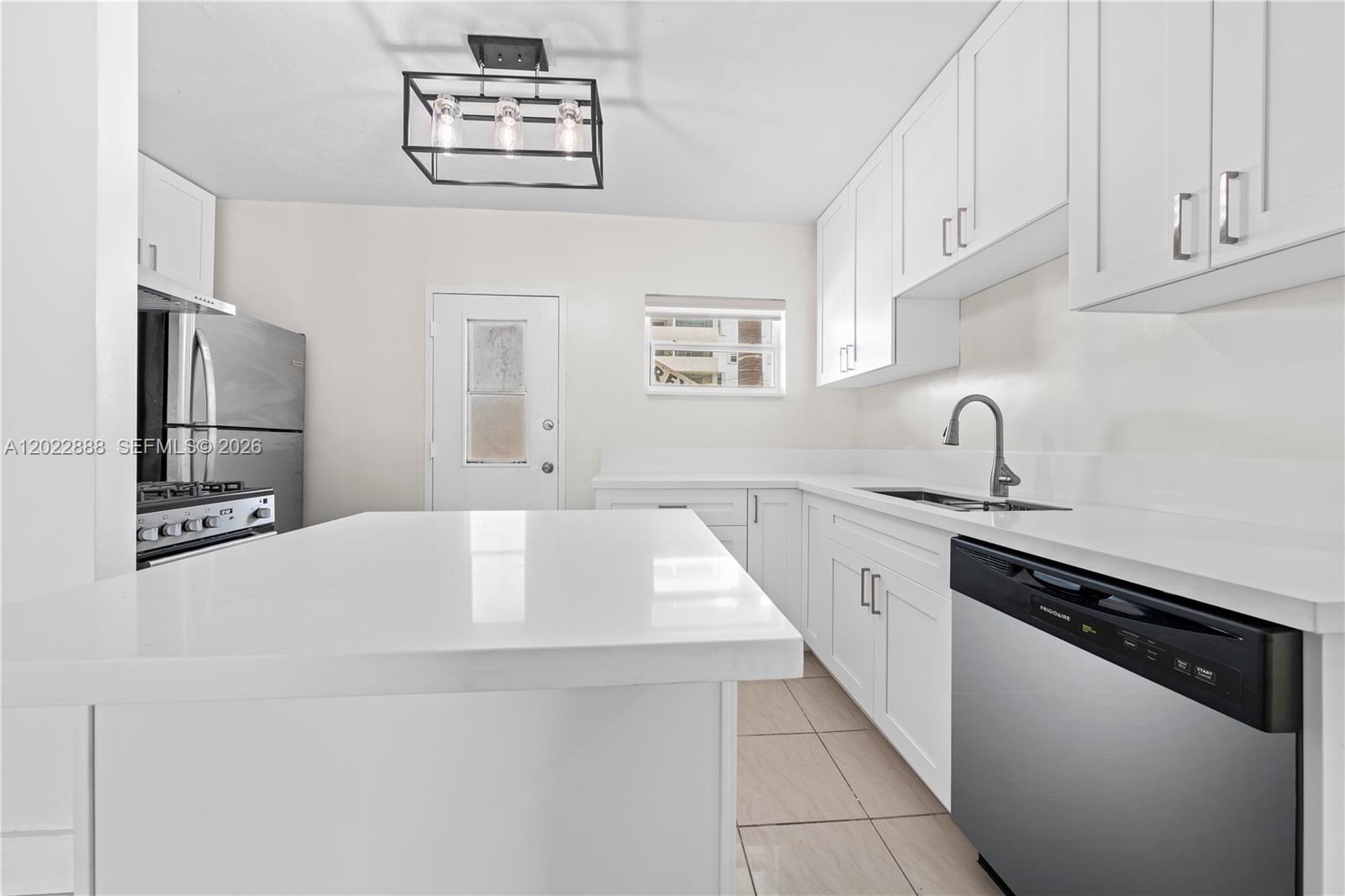 A modern kitchen features white cabinetry, a central island, and stainless steel appliances — 1300 Lincoln Rd # D204, Miami Beach FL 33139, MIAMI BEACH, FL