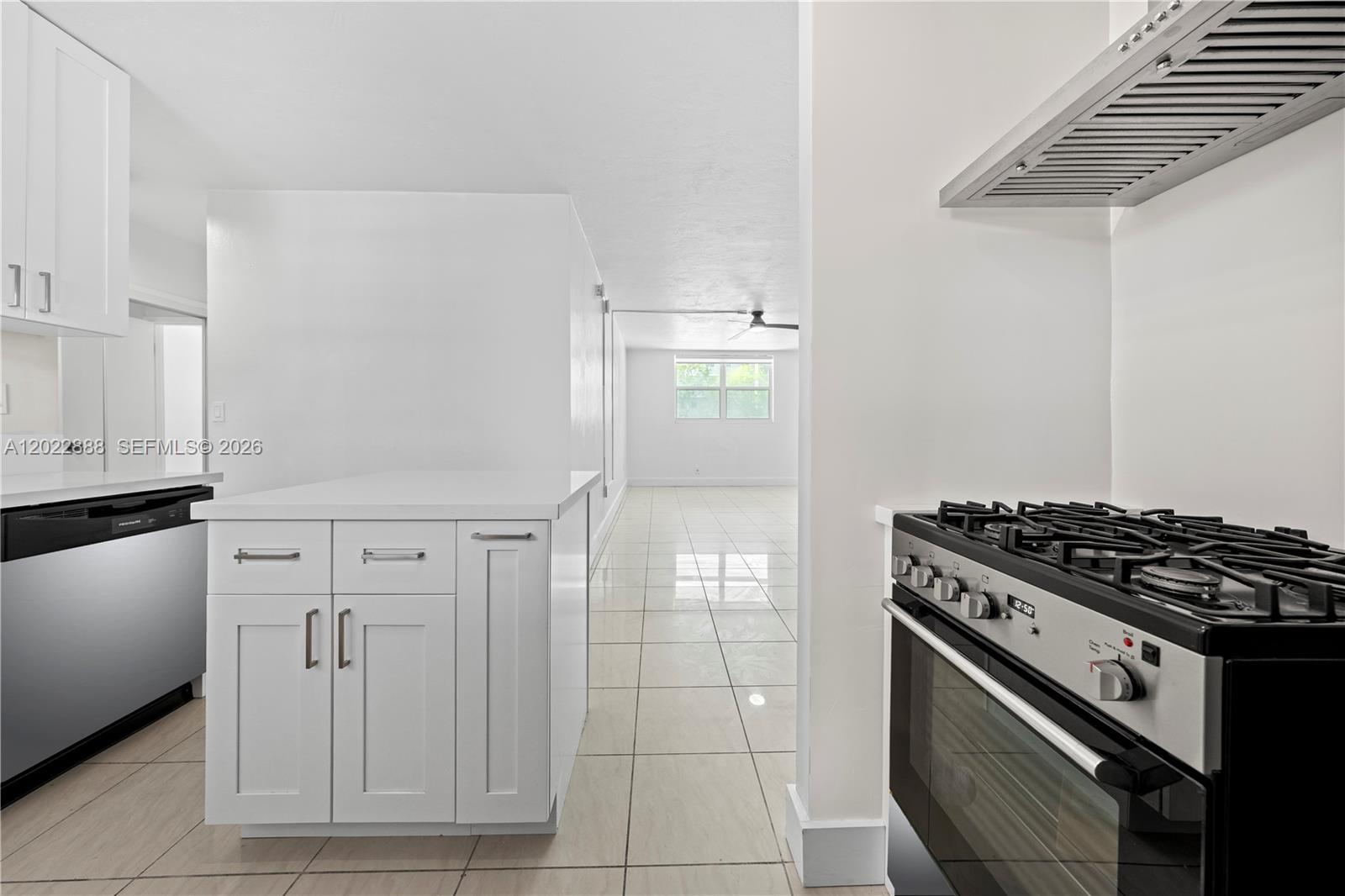 A kitchen with white cabinets and stainless steel appliances opens into a tiled living area — 1300 Lincoln Rd # D204, Miami Beach FL 33139, MIAMI BEACH, FL