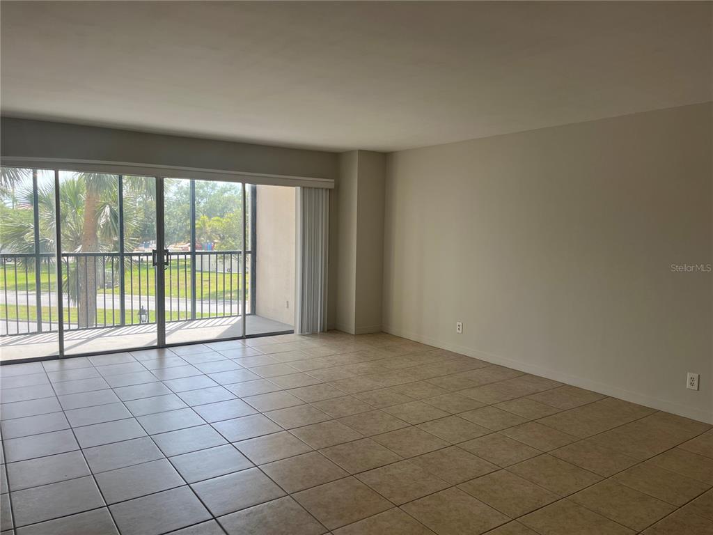 An empty room with beige tile flooring and a sliding glass door leading to a balcony — 10355 PARADISE BOULEVARD UNIT 113, TREASURE ISLAND, FL