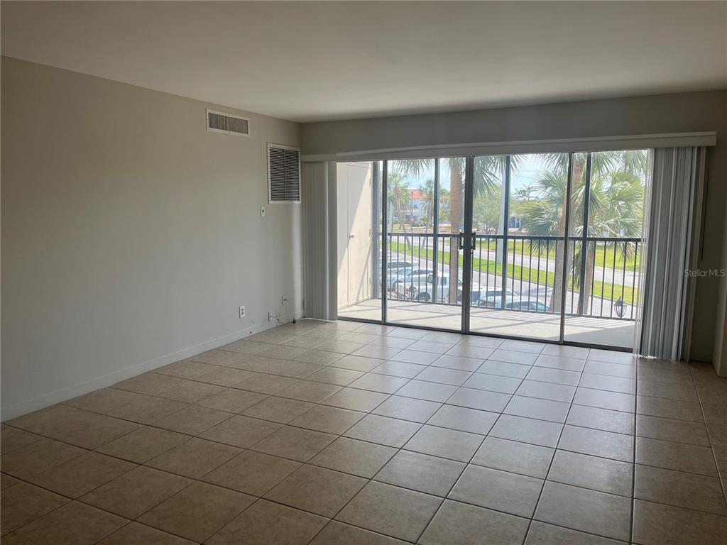 An empty room with beige tile flooring, white walls, and a large sliding glass door — 10355 PARADISE BOULEVARD UNIT 113, TREASURE ISLAND, FL