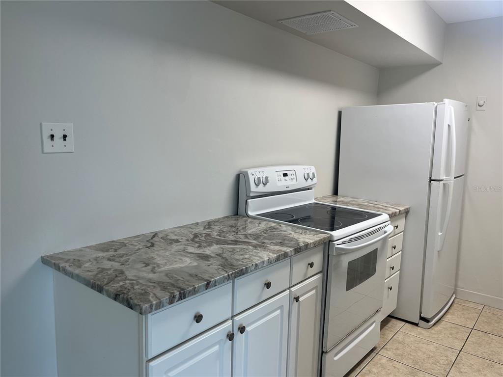 A kitchen features white cabinets, a marble-patterned countertop, a white stove, and a refrigerator — 10355 PARADISE BOULEVARD UNIT 113, TREASURE ISLAND, FL