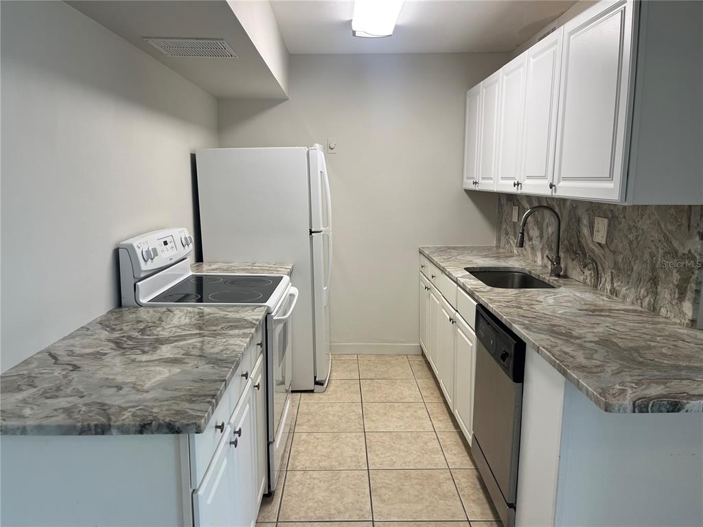 A galley kitchen features white cabinets, granite countertops, and stainless steel appliances — 10355 PARADISE BOULEVARD UNIT 113, TREASURE ISLAND, FL