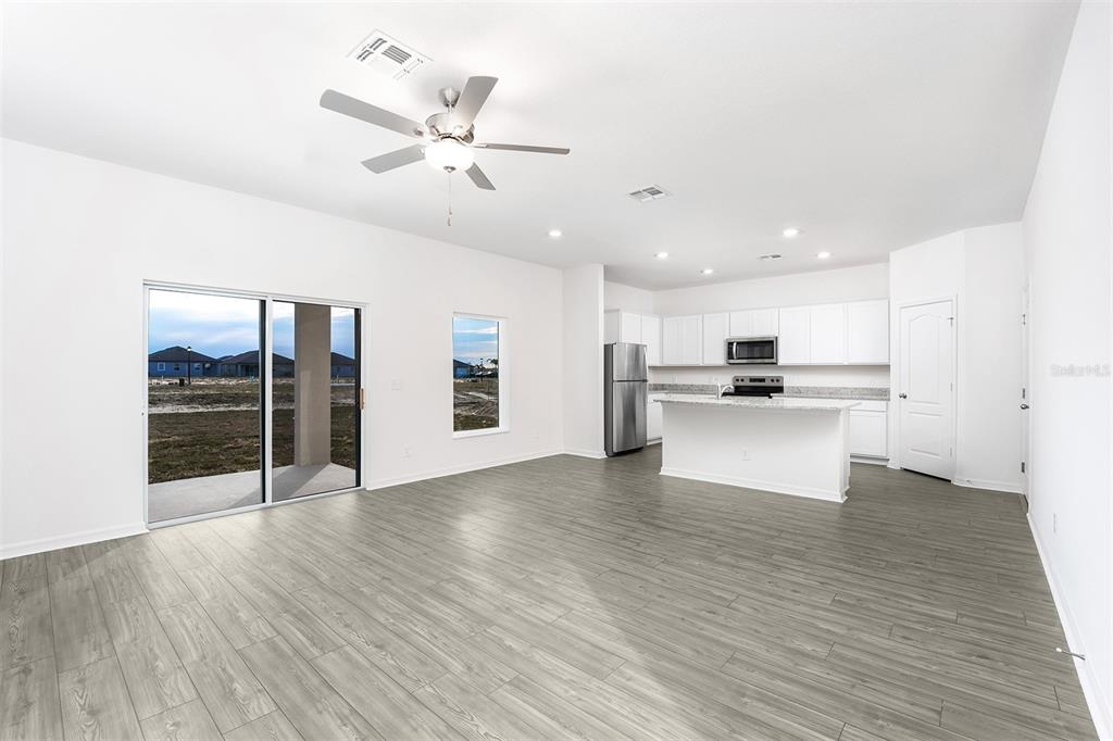 An open-concept kitchen and living area features white cabinetry, stainless steel appliances, and wood-look flooring — 3719 BERGAMOT STREET, LAKE ALFRED, FL