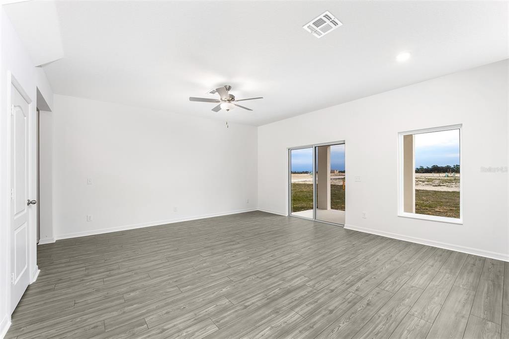 An empty room with gray wood-look flooring, a ceiling fan, sliding glass doors, and windows — 3719 BERGAMOT STREET, LAKE ALFRED, FL
