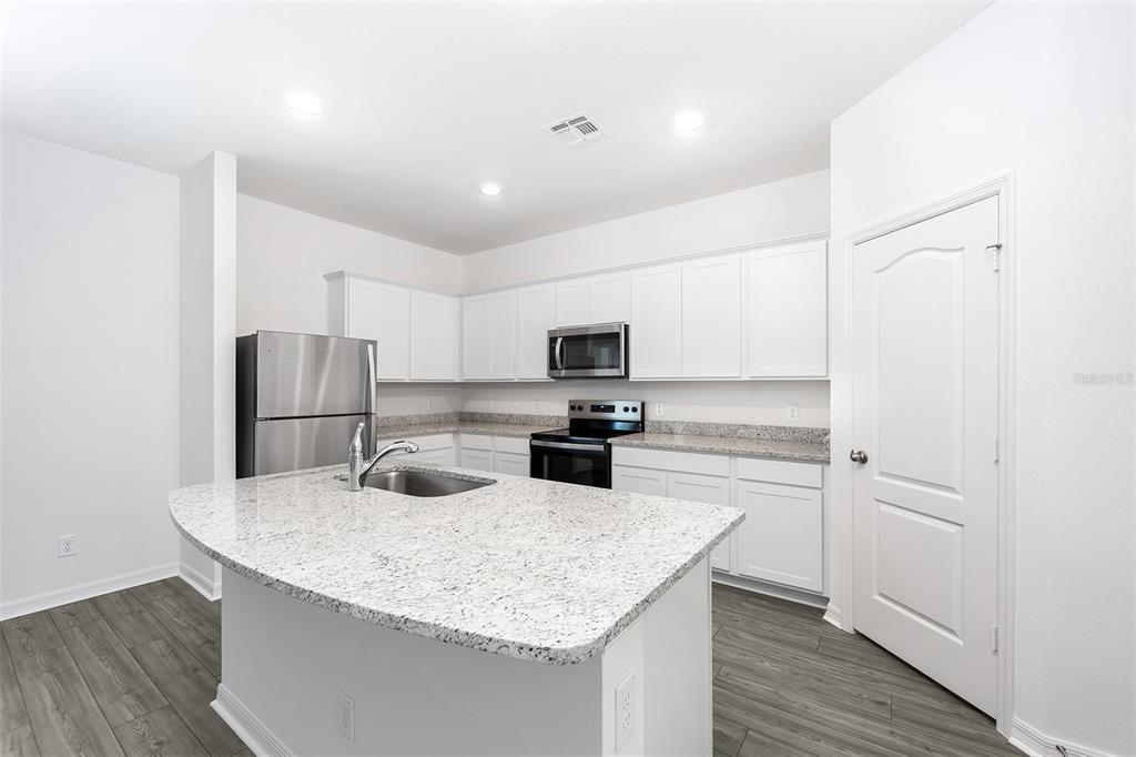 A kitchen features white cabinets, granite countertops, stainless steel appliances, and a central island — 3719 BERGAMOT STREET, LAKE ALFRED, FL