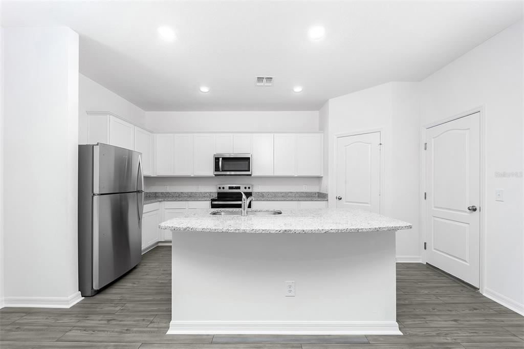 A kitchen with white cabinets, granite countertops, stainless steel appliances, and a central island — 3719 BERGAMOT STREET, LAKE ALFRED, FL