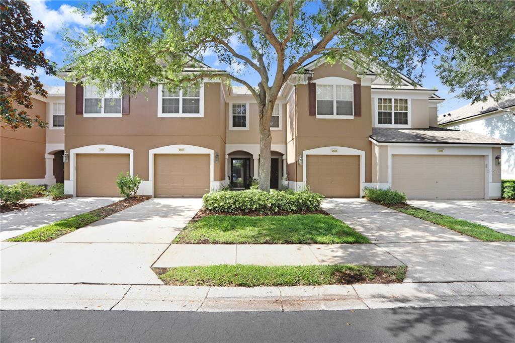 A multi-unit townhouse building with four garage doors and a large central tree — 4986 POND RIDGE DRIVE, RIVERVIEW, FL
