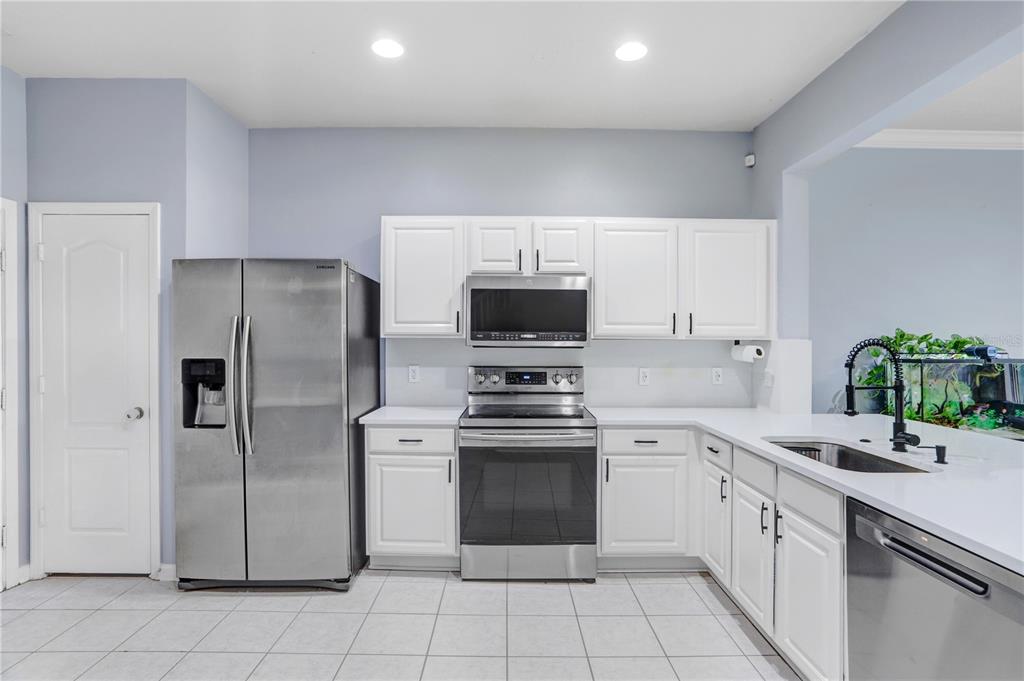 A kitchen features white cabinets, stainless steel appliances, and light-colored tile flooring — 4986 POND RIDGE DRIVE, RIVERVIEW, FL