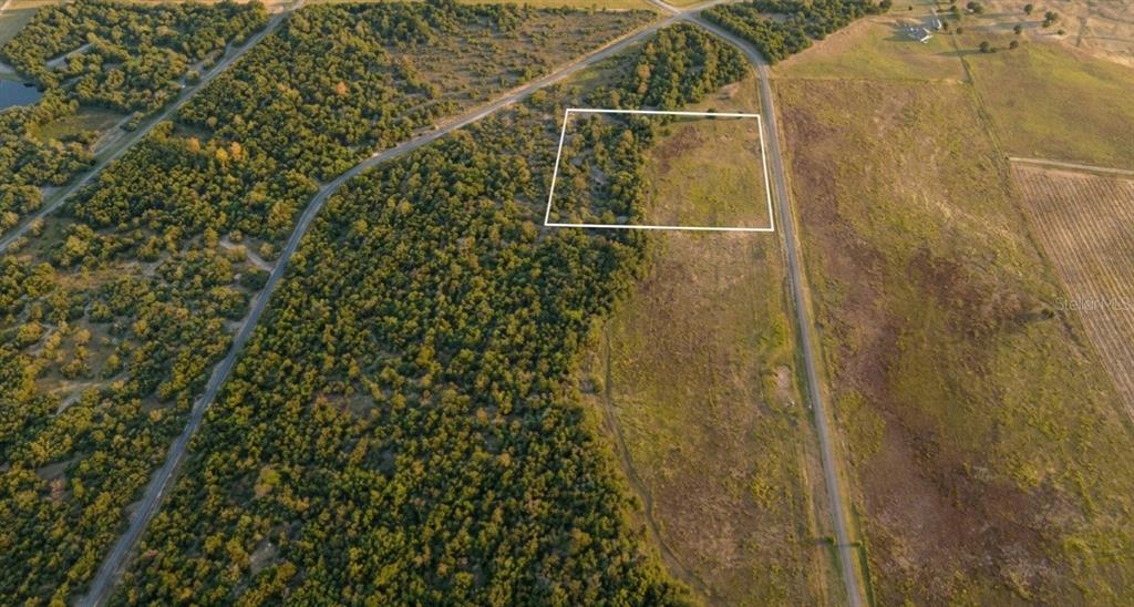 An aerial view shows a large, undeveloped plot of land bordered by roads and trees — SE 136TH TERRACE, MORRISTON, FL