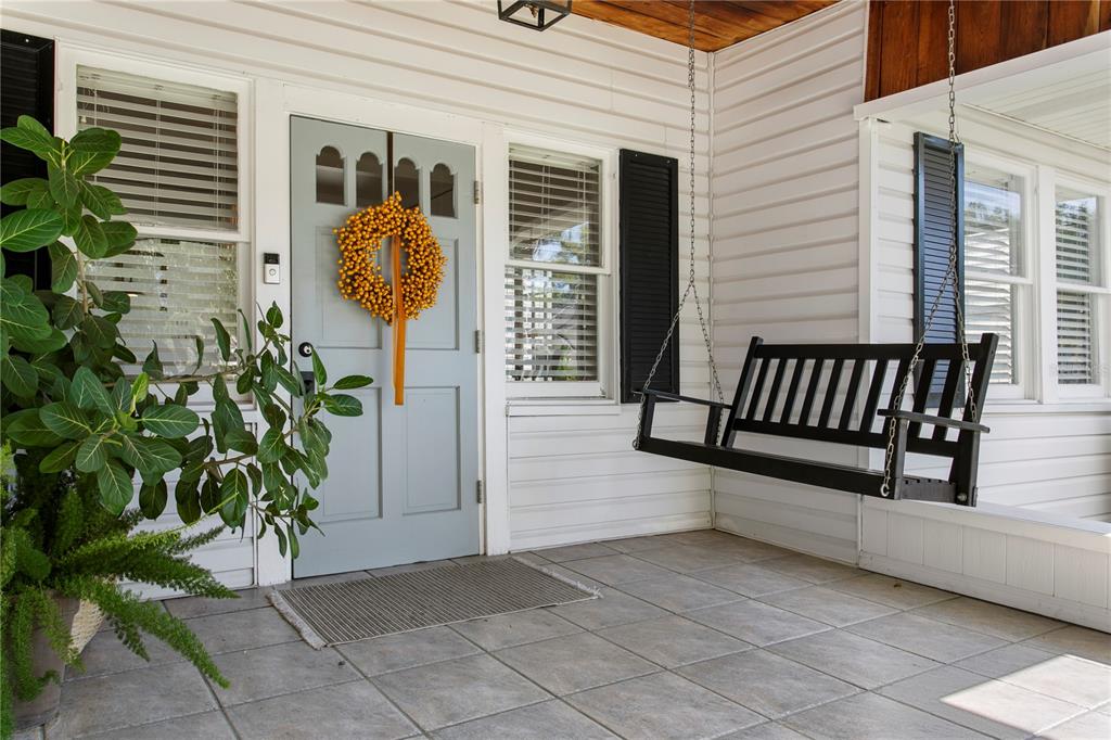 A covered front porch features a light blue door, a black porch swing, and tile flooring — 3407 W SAN PEDRO STREET, TAMPA, FL