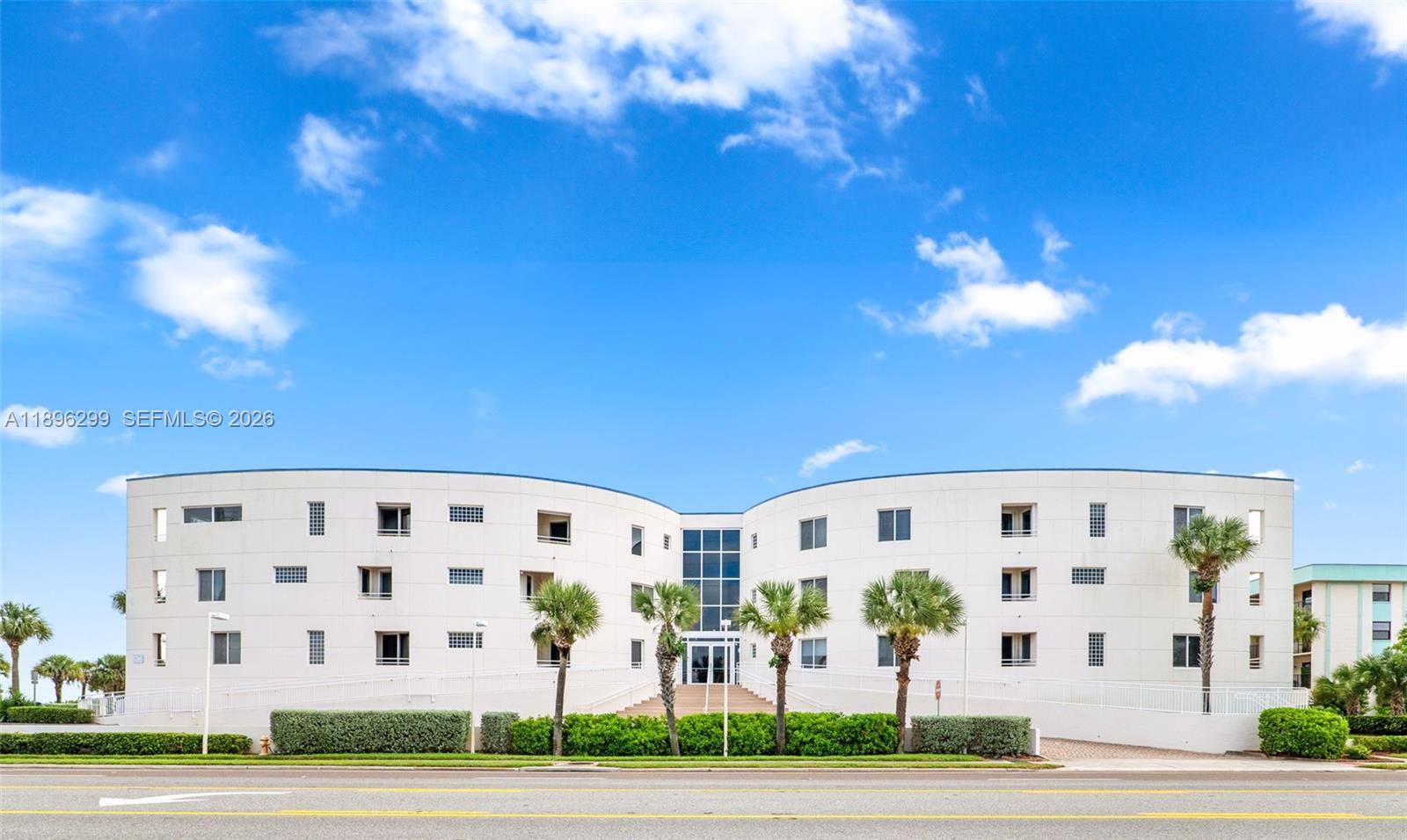 A white, multi-story building with a curved facade stands behind a row of palm trees — 601 N Miramar # 107, Indialantic FL 32903, INDIALANTIC, FL