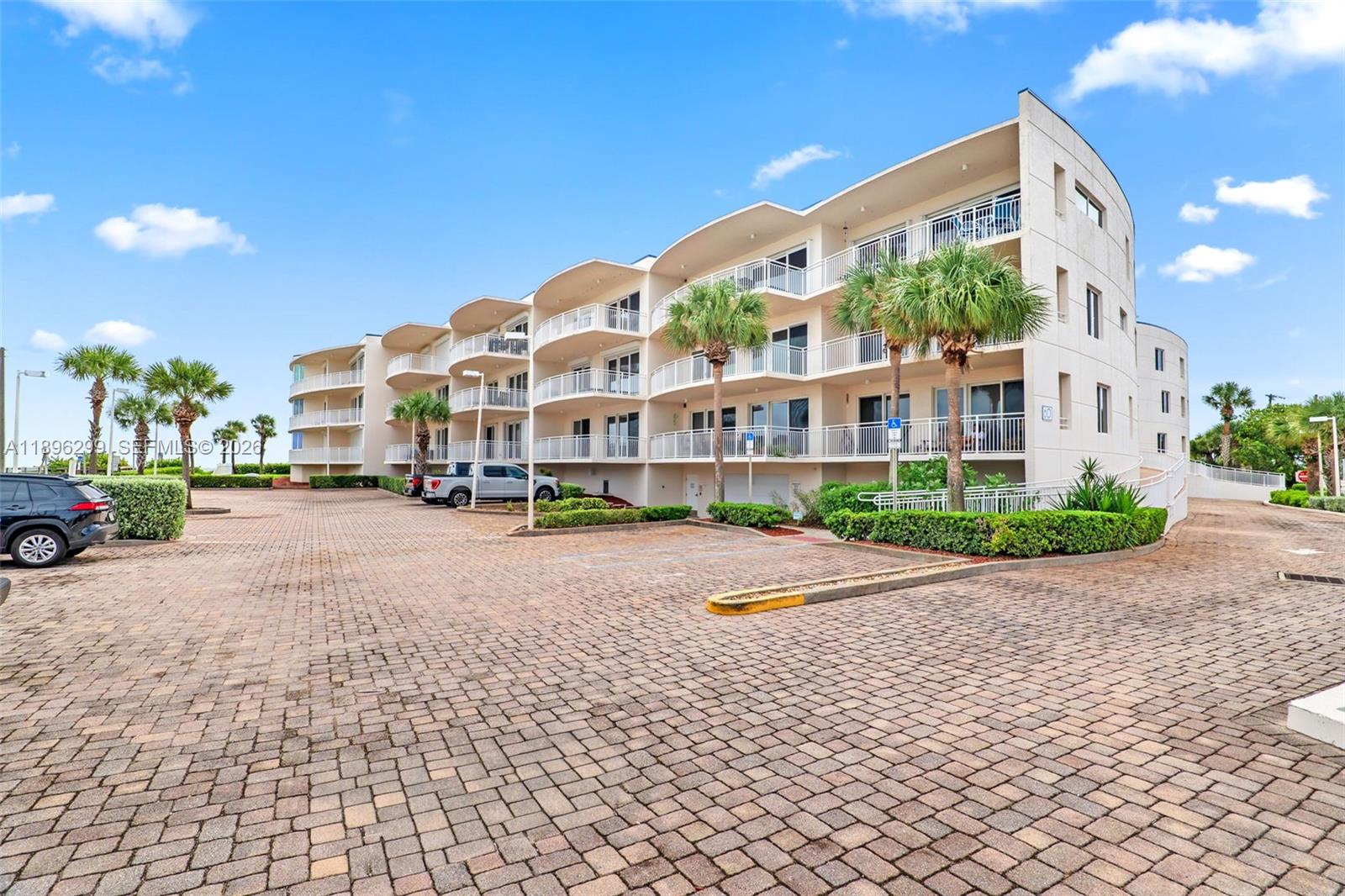A multi-story apartment building with curved balconies sits above a paved parking lot — 601 N Miramar # 107, Indialantic FL 32903, INDIALANTIC, FL