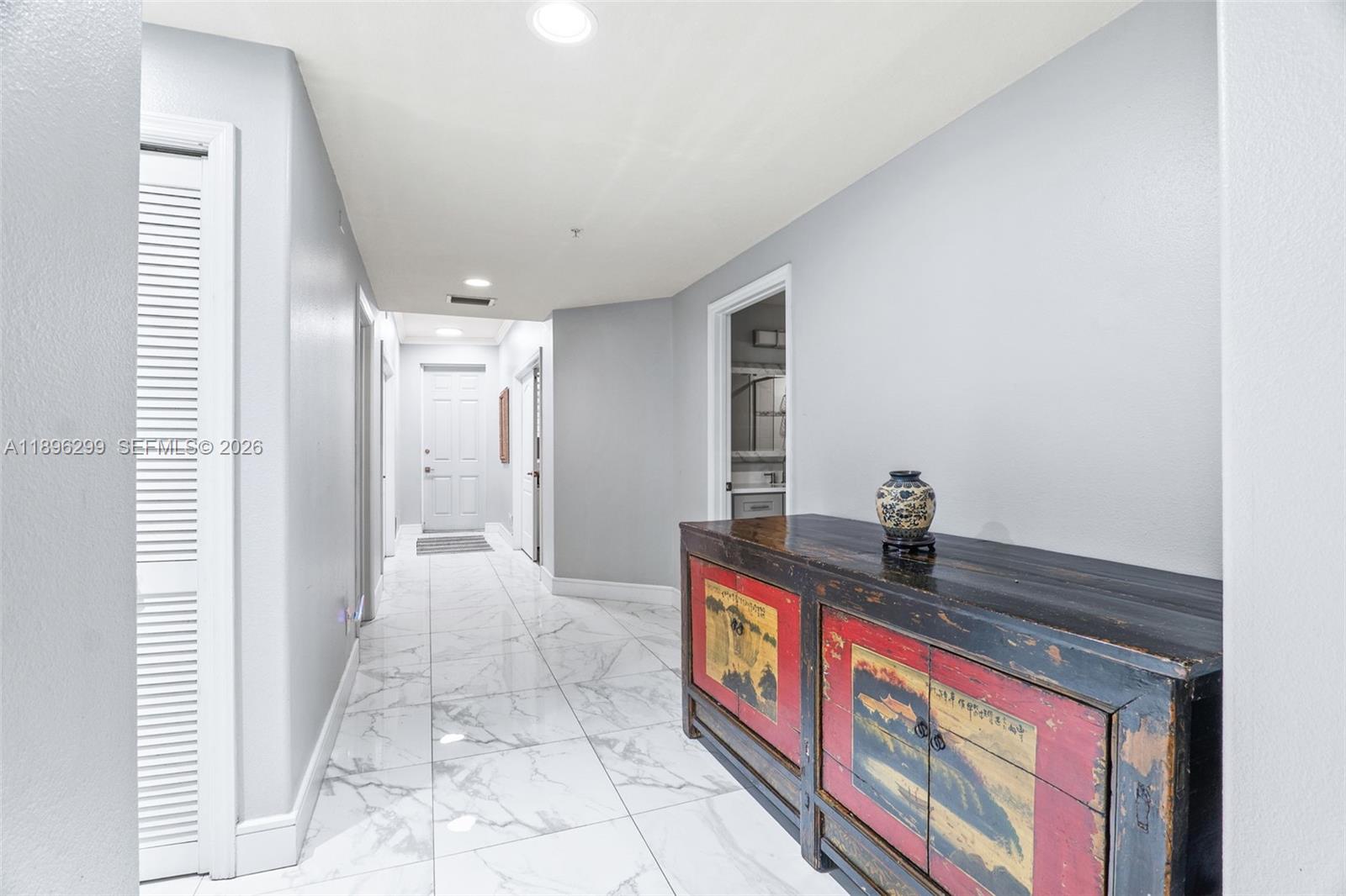 A hallway with white marble-look tile flooring features a decorative Asian-style cabinet on the right — 601 N Miramar # 107, Indialantic FL 32903, INDIALANTIC, FL