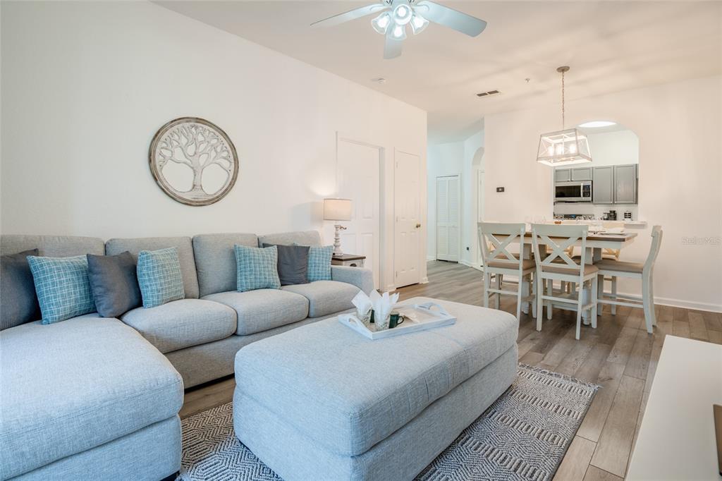 A living room with a gray sectional sofa, ottoman, and an adjacent dining area — 2303 BUTTERFLY PALM WAY UNIT 303, KISSIMMEE, FL