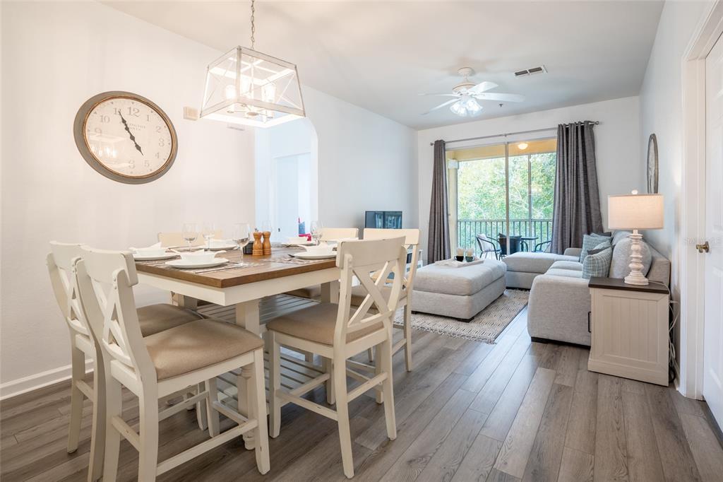 A dining area with a wooden table and chairs sits adjacent to a living room — 2303 BUTTERFLY PALM WAY UNIT 303, KISSIMMEE, FL