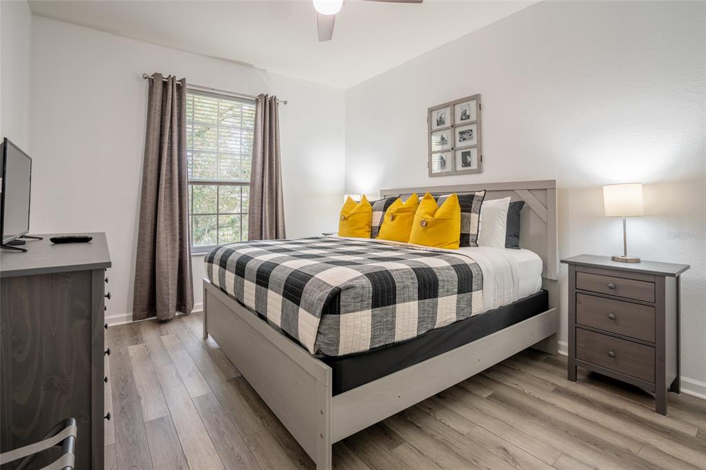 A bedroom features a bed with a buffalo check quilt, yellow pillows, and wood furniture — 2303 BUTTERFLY PALM WAY UNIT 303, KISSIMMEE, FL