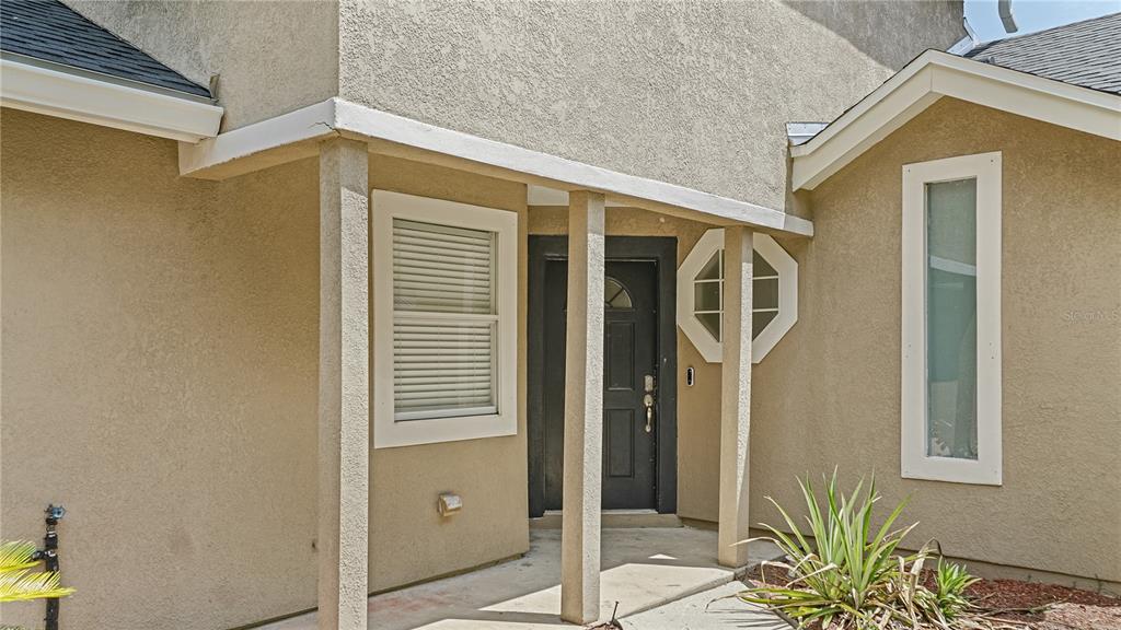 The exterior of a house features a covered entryway with a black door and stucco — 1769 SADDLEBACK RIDGE ROAD, APOPKA, FL